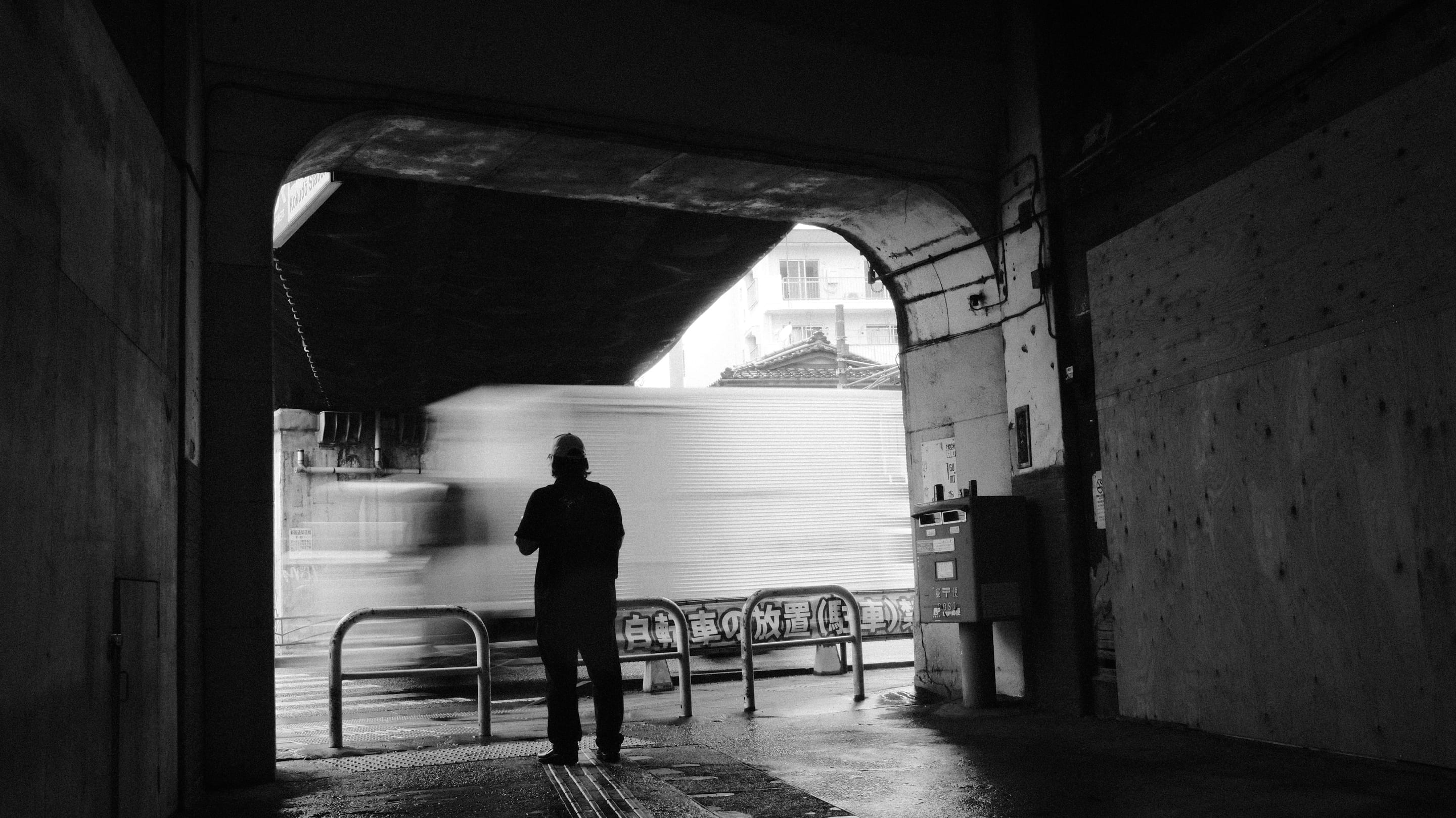 A man at the mouth of the tunnel, sharp and still, a truck passing as pure blur